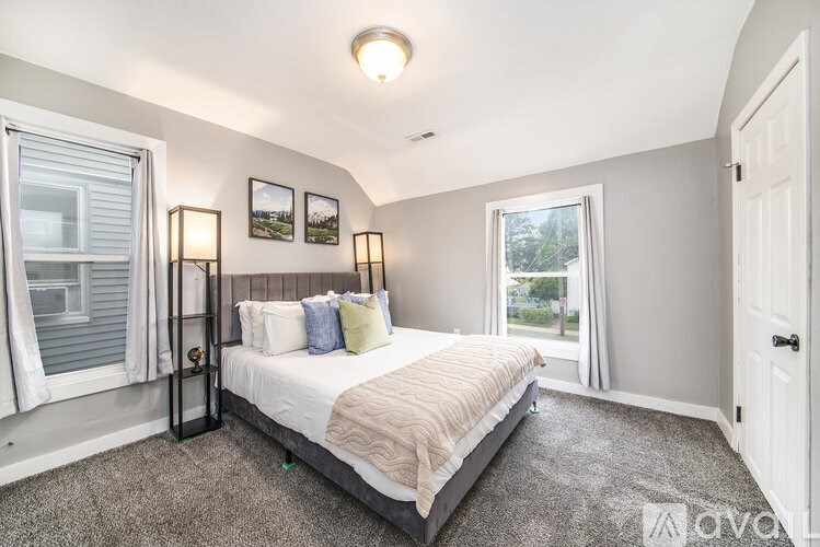 A bedroom with a large bed and a window with white curtains.