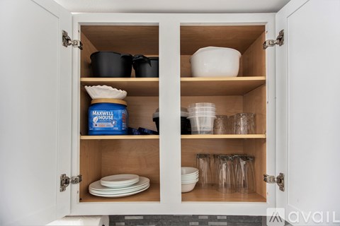 A kitchen cabinet with a white door is open, revealing a variety of cookware and glasses inside.