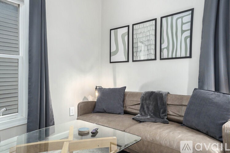 A living room with a couch, a glass table, and three abstract paintings on the wall.