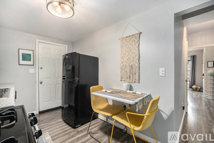 A kitchen with a black fridge, a yellow chair and a table with a woven bag hanging on the wall.