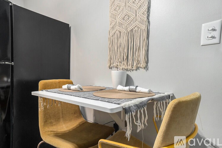 A table with a blanket on it and two chairs in front of a fridge.