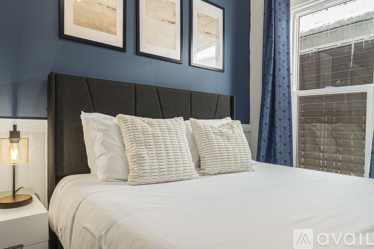 A bed with white pillows and a grey headboard with a lamp on the side table.