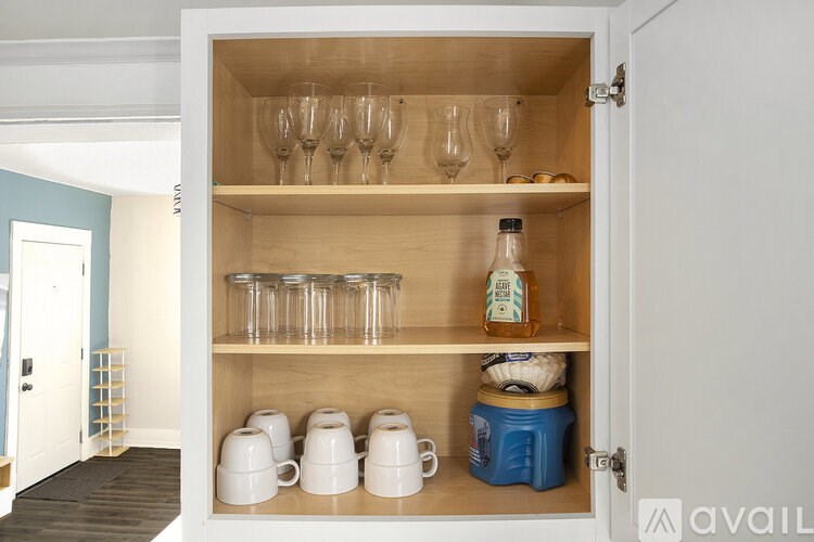 A kitchen cabinet with glasses, cups and a bottle.