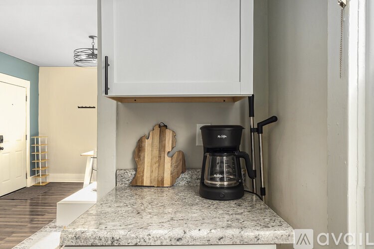 A kitchen counter with a coffee maker and wooden cutting board.
