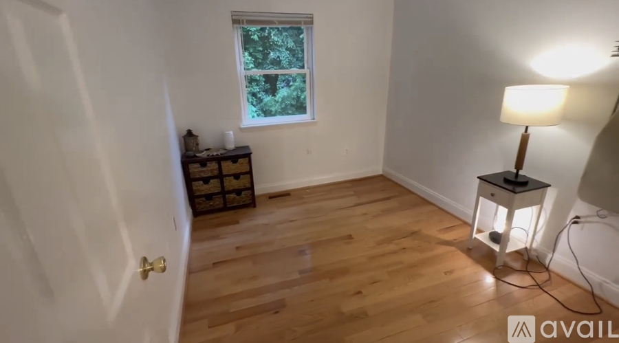 A room with wooden flooring and a window with a view of trees.