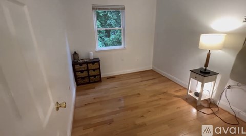 A room with wooden flooring and a window with a view of trees.
