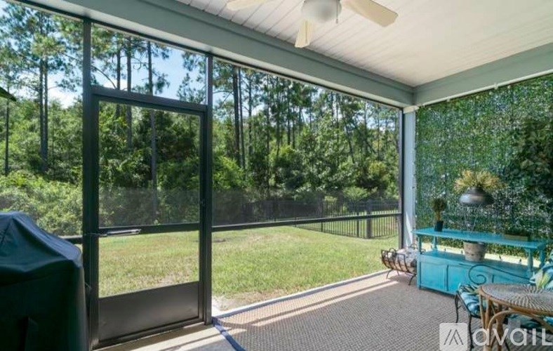 A screened porch with a ceiling fan and a view of a green lawn and trees.