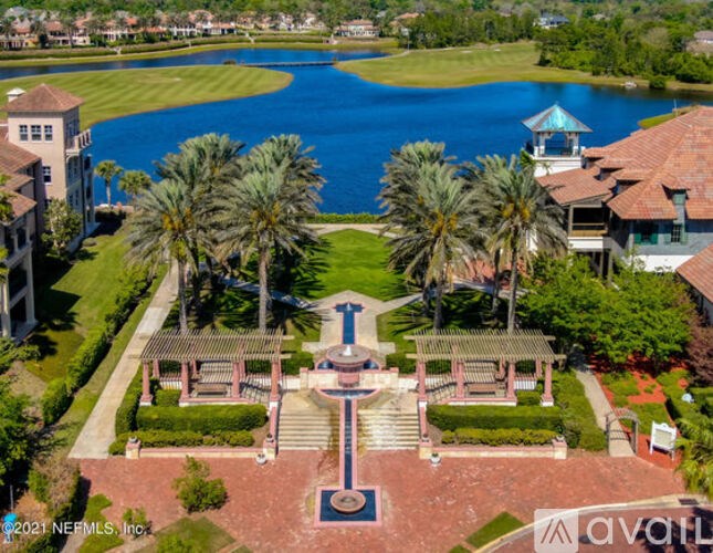 A beautiful aerial view of a park with a fountain, palm trees, and a lake.