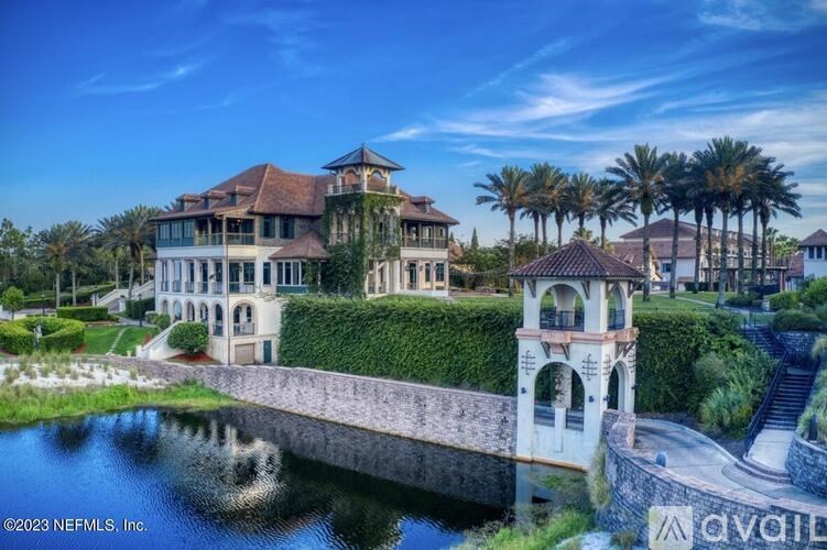 A large, luxurious house with a tower and a bridge over a pond.
