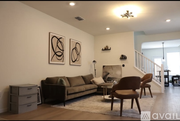 A living room with a brown couch, two chairs, and two framed pictures on the wall.