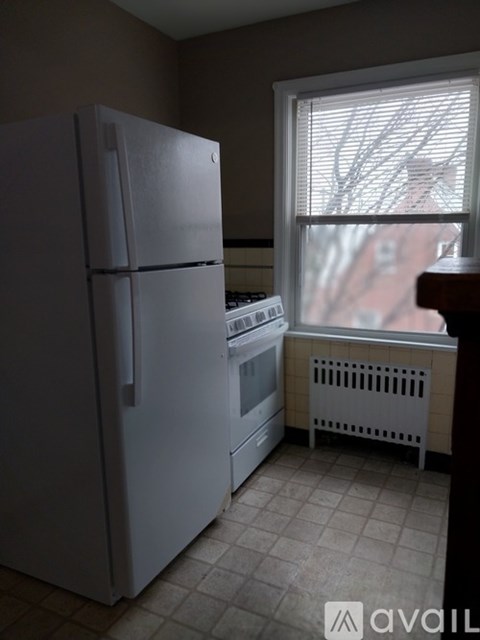 A white refrigerator stands in a kitchen next to a window.