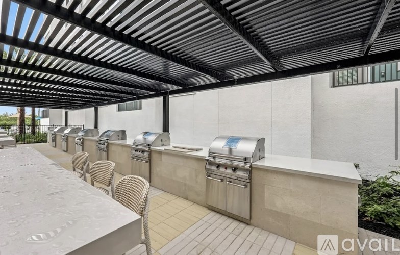 A patio with a row of grills and chairs under a roof.