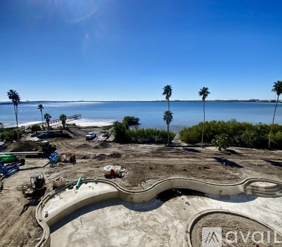 A construction site with a large swimming pool in the foreground and palm trees in the background.