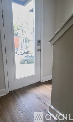 A white door with a glass window showing a car and trees outside.