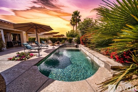 A pool surrounded by palm trees and flowers at sunset.
