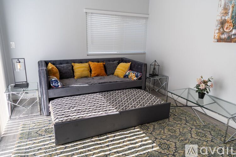 A grey couch with yellow pillows sits in a room with a glass table and a painting on the wall.