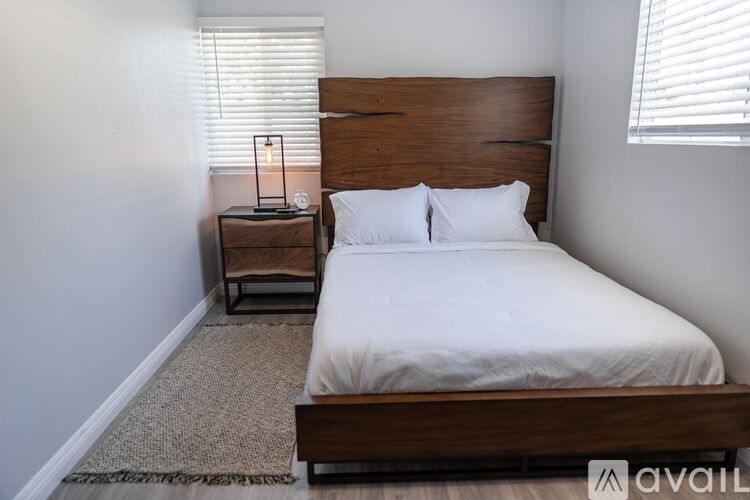 A bedroom with a large bed and a small table with a lamp on it.