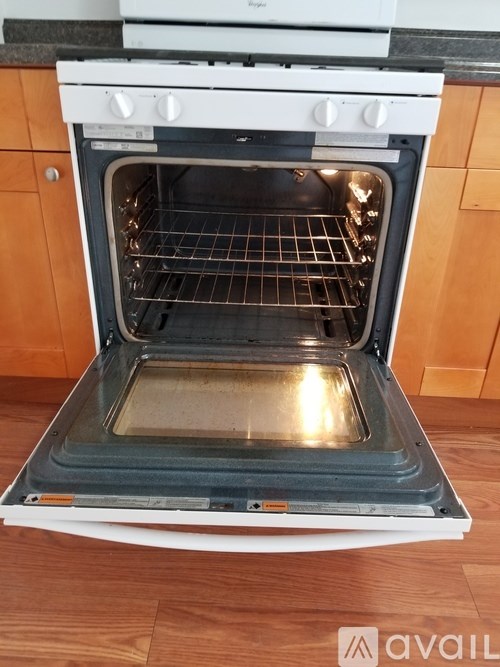 An oven with the door open is sitting on a wooden floor.