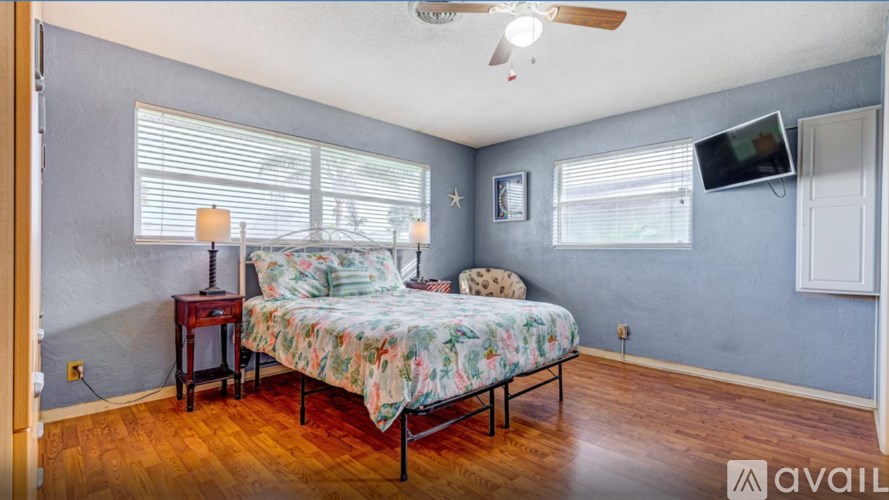 A bedroom with a bed, a ceiling fan, and a television mounted on the wall.
