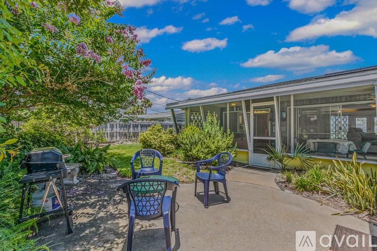 A patio with chairs and a grill is surrounded by greenery.