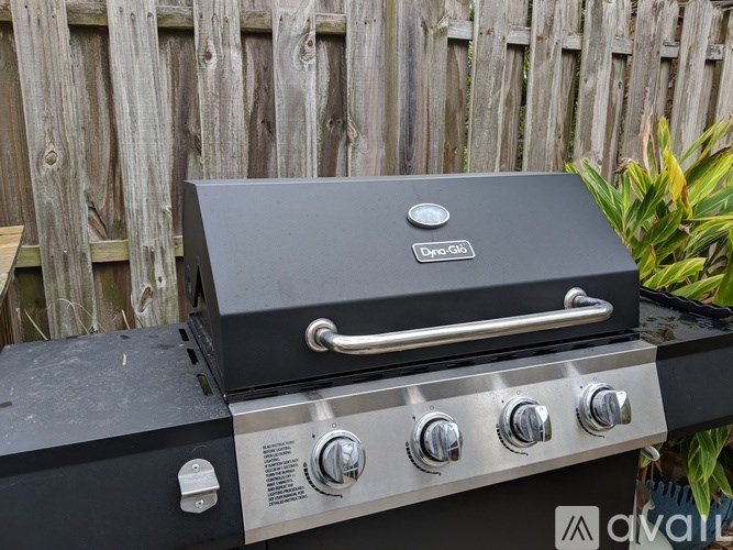 A DynoGlo grill with four burners and a side handle is placed on a wooden fence.