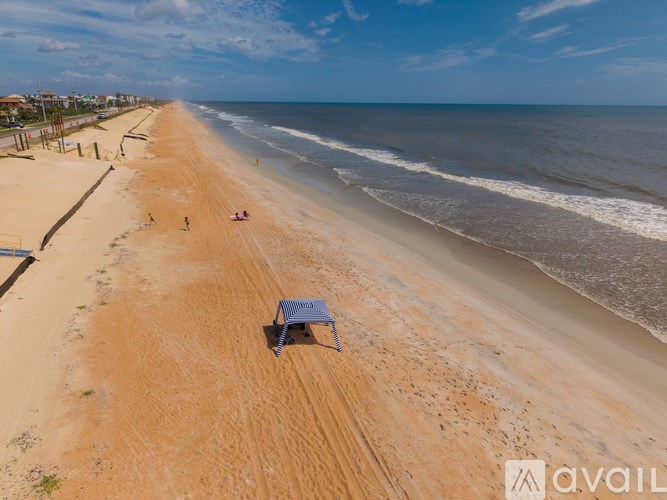 An empty beach with a blue umbrella and a few people.