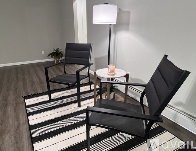 A black chair is placed in front of a white lamp and a small table with a lit candle on it.