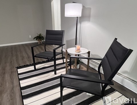 A black chair is placed in front of a white lamp and a small table with a lit candle on it.
