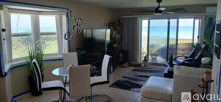A living room with a television, chairs, and a view of the beach.