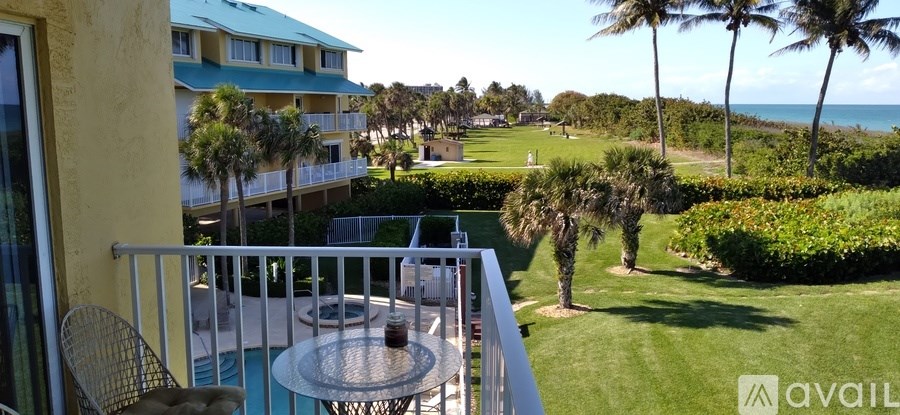 A balcony with a table and chairs overlooks a lush green lawn and palm trees.