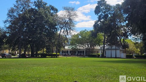 A grassy field with trees and a house in the background.