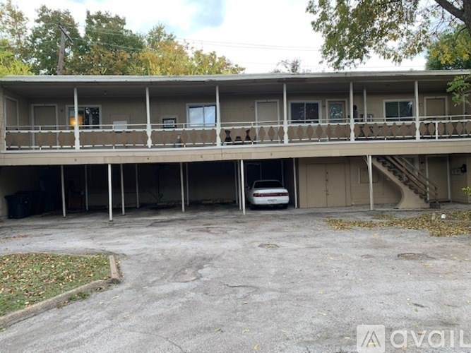 A car is parked in a parking lot in front of a two-story apartment building.