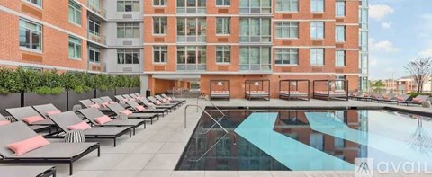 A large pool surrounded by lounge chairs in front of a red brick building.