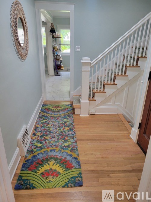 A hallway with a wooden staircase and a colorful rug.