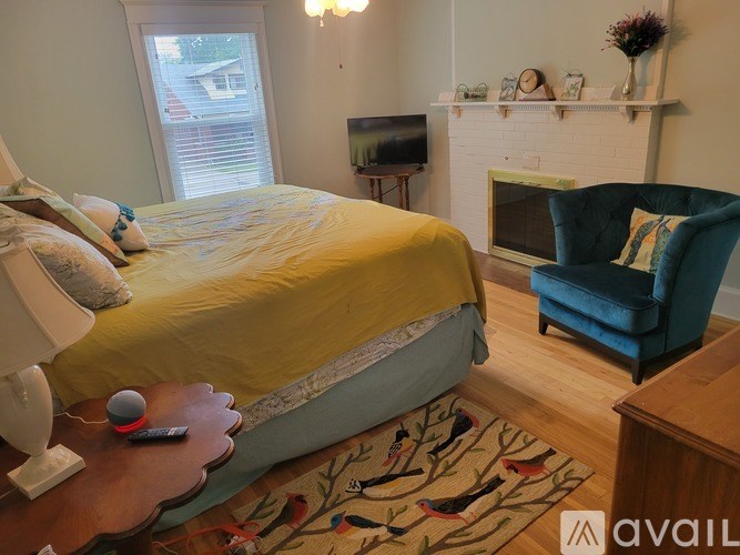 A bedroom with a bed, chair, and fireplace.