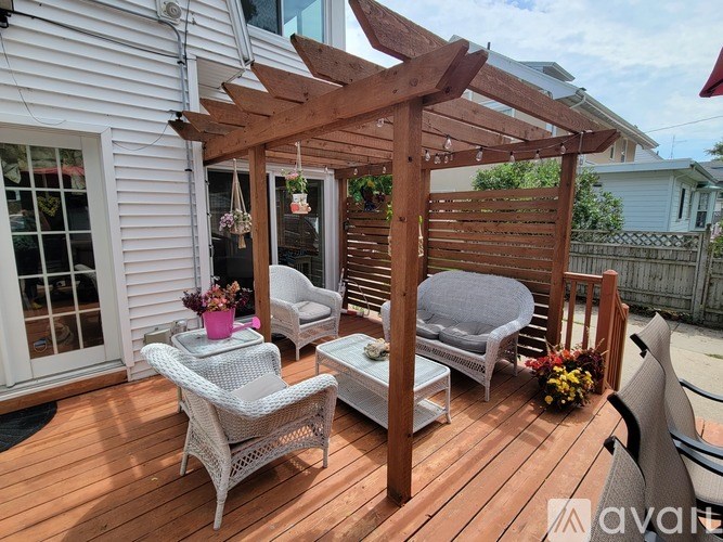 A wooden pergola with a white wicker chair and a small table is on a wooden deck.
