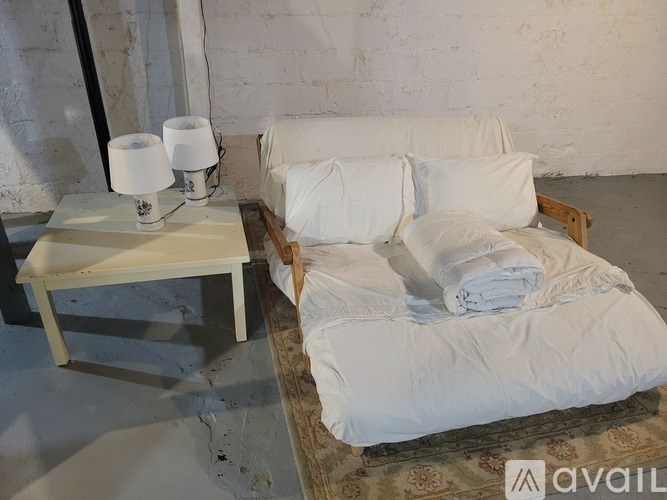 A white bed with a white pillow and a white chair with a white cushion.