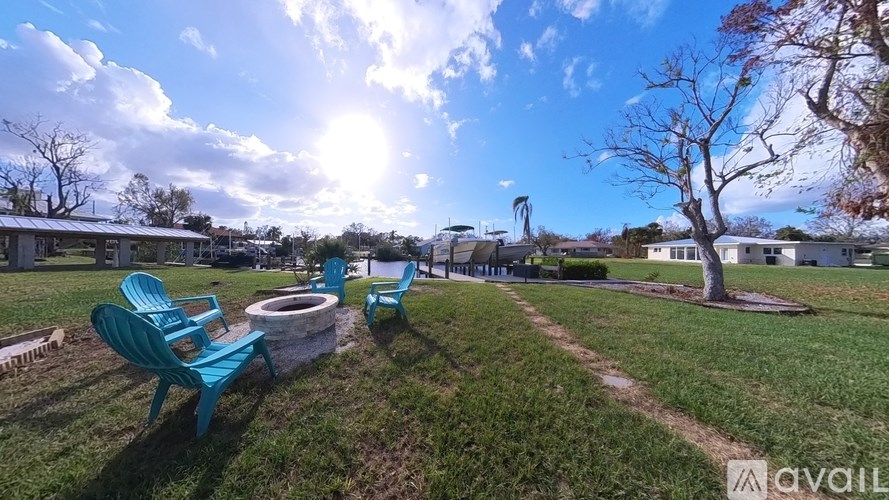 A sunny day at the park with blue chairs and a fire pit.