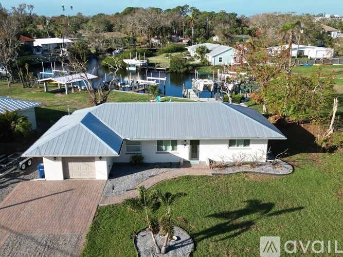 A house with a grey roof and white walls is surrounded by a green lawn.