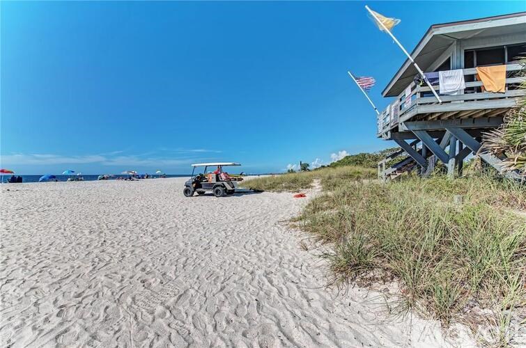 A beach scene with a blue house and a golf cart on the sand.