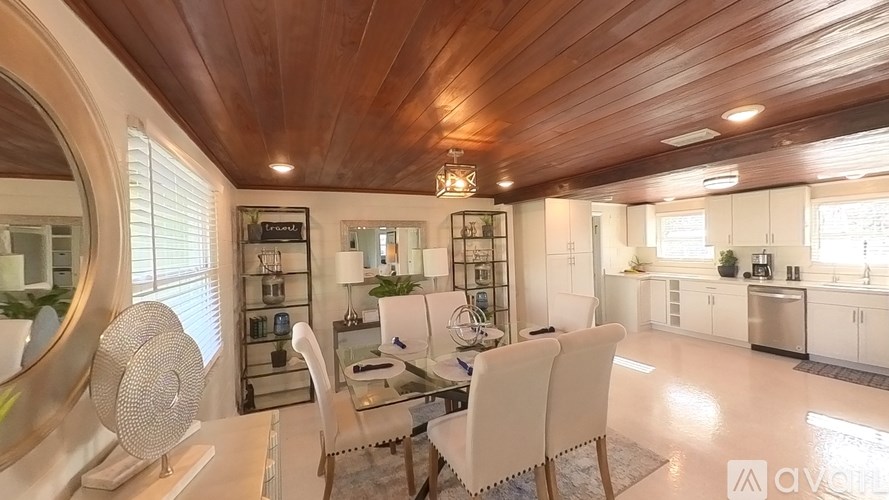 A modern kitchen with white chairs and a wooden ceiling.
