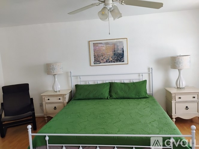 A bedroom with a green bedspread and a white bed.