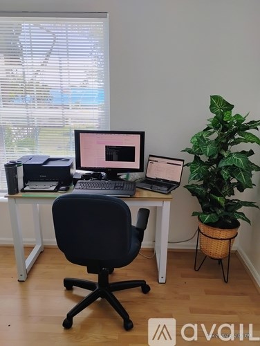 A black chair is in front of a desk with a laptop and a monitor.