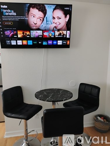 A flat screen TV mounted on a wall above a round table with two black chairs.