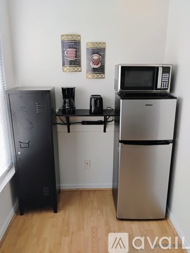 A kitchen with a black fridge, a black computer tower, a microwave on top of the fridge, and a coffee maker on a shelf.