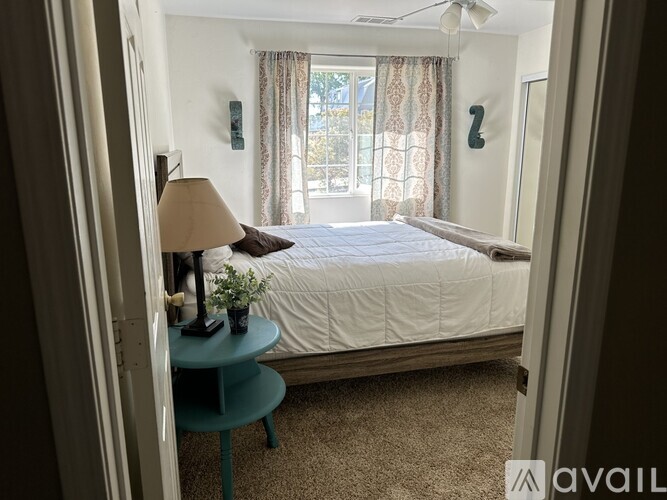 A bedroom with a bed, a nightstand with a lamp, and a window with curtains.
