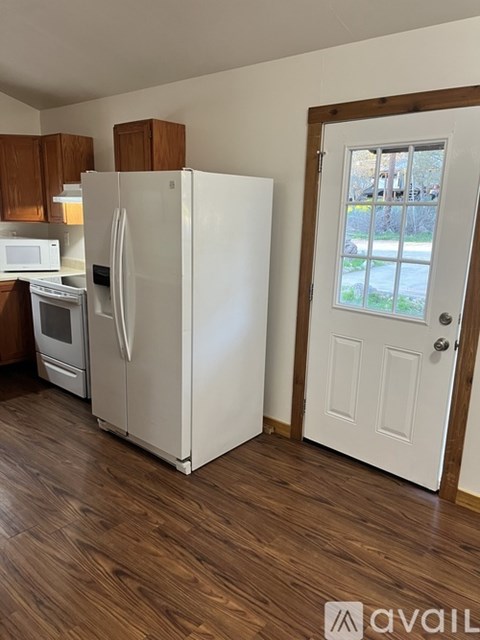 A white refrigerator stands in a kitchen with wooden cabinets and a white door.