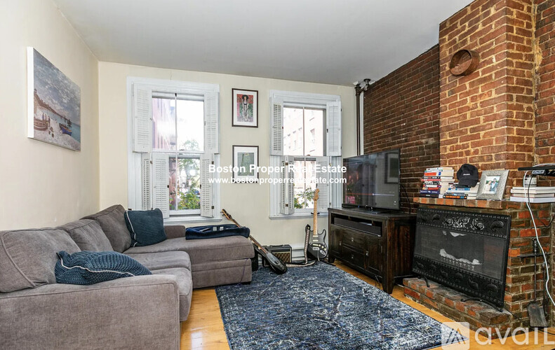 A living room with a grey couch, a black fireplace, and a blue rug.