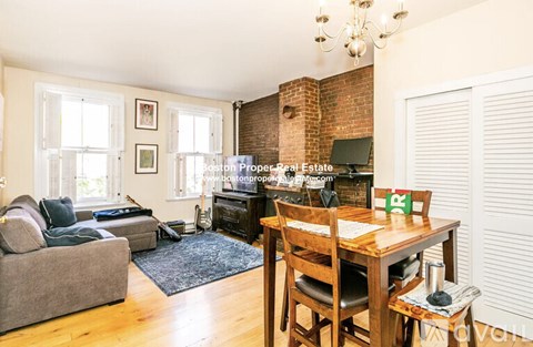 A living room with a brick fireplace and a dining table set up.