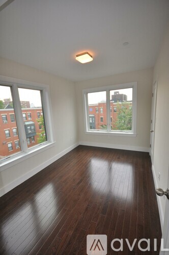 A room with wooden floors and two windows overlooking a city.